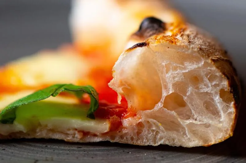Gros plan sur le cornicione alvéolé et doré d'une pizza Contemporanea